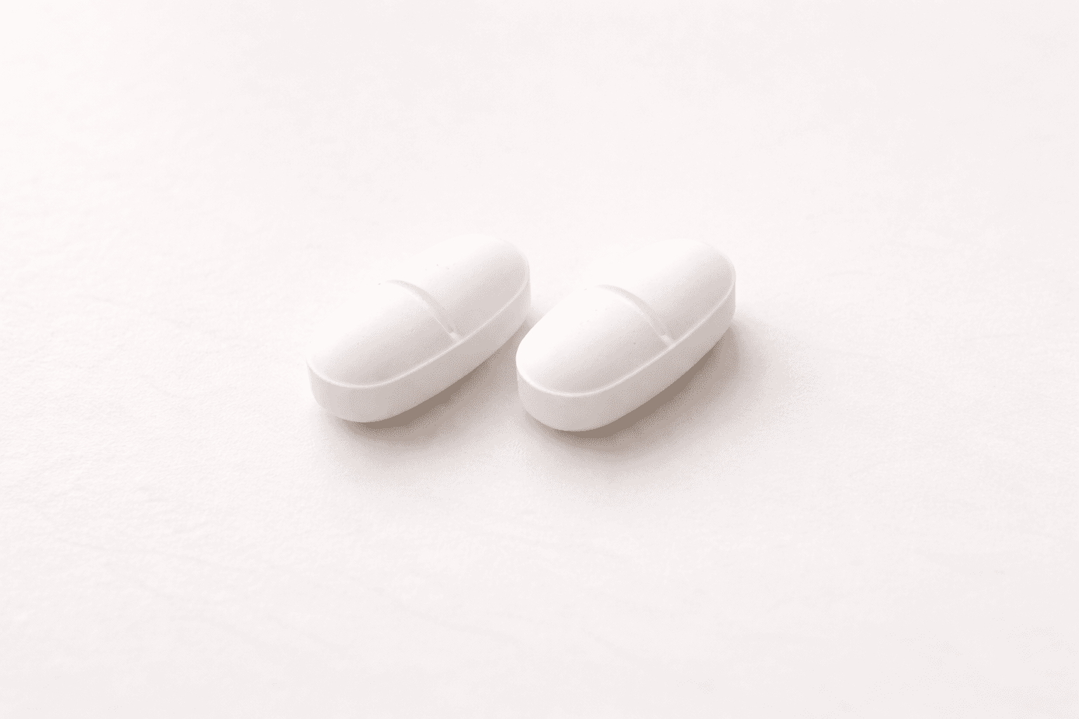 Dois comprimidos brancos sobre fundo branco, representando os novos medicamentos orais GLP-1 para emagrecer